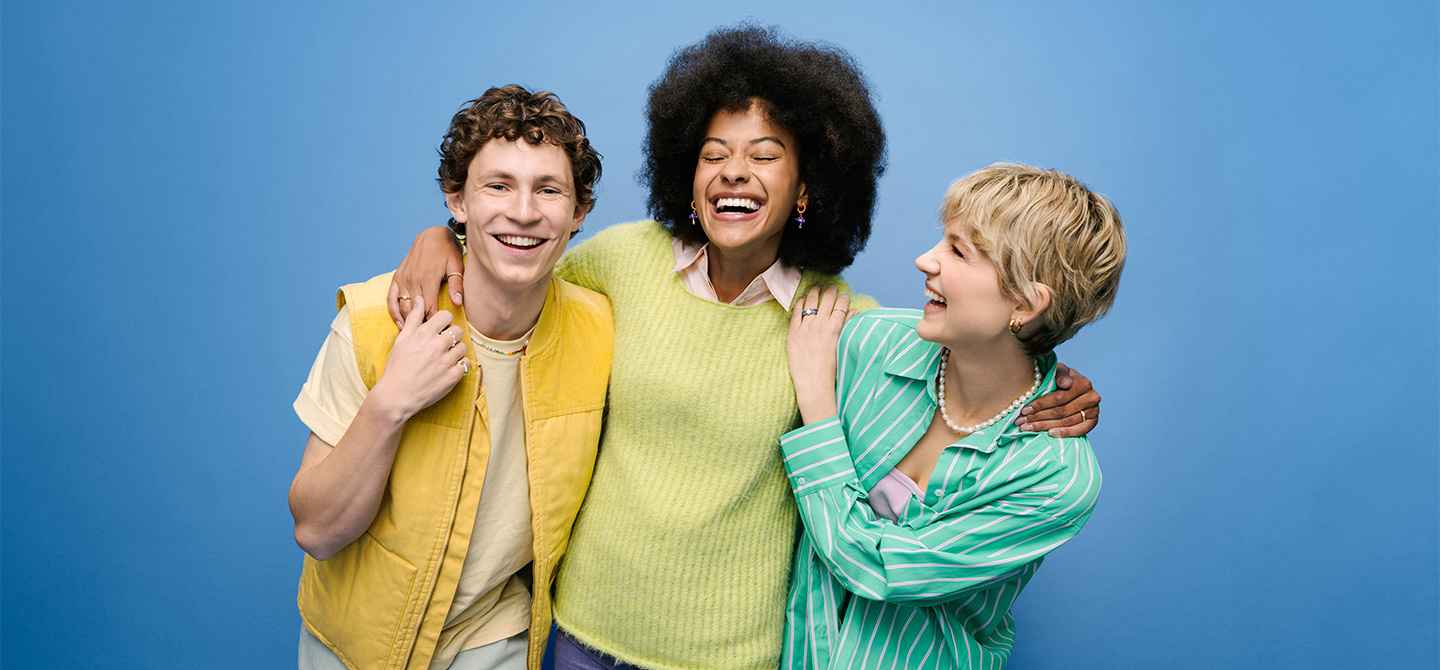 Drei junge Menschen umarmen sich und lachen.