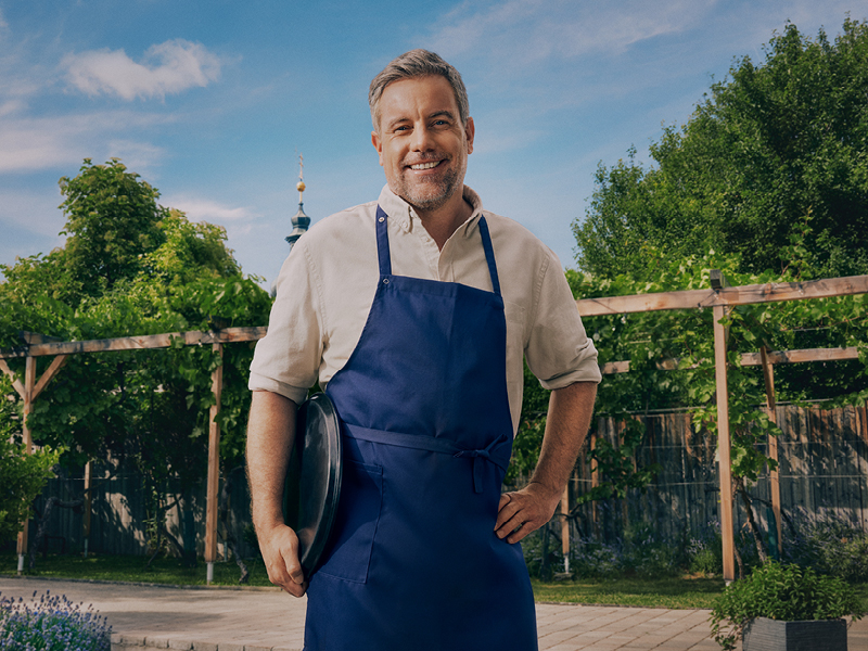 Ein Mann in einer blauen Schürze mit einem Tablett unter dem Arm.