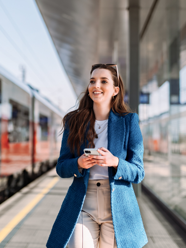 Eine Frau geht auf dem Bahnsteig. Sie hat ein Mobiltelefon in der Hand.